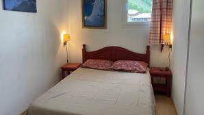 Un dormitorio con una cama, dos mesitas de noche, una ventana con cortinas y dos lámparas de pared.