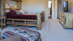 A rustic bedroom with a wooden bed frame, a television on a wooden dresser, and a patterned rug. - Eden/Powder Mountain/Snowbasin: mountain getaway, skiing, hiking, biking, golf (Eden)