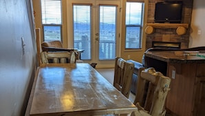 A dining area with a long wooden table and rustic chairs, a stone fireplace, and a television mounted above it. - Eden/Powder Mountain/Snowbasin: mountain getaway, skiing, hiking, biking, golf (Eden)