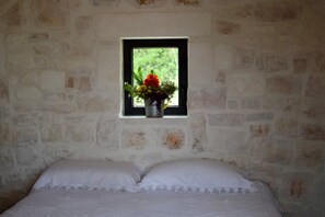 A room with a bed, a window with a view of greenery, and a small window with a flower pot.