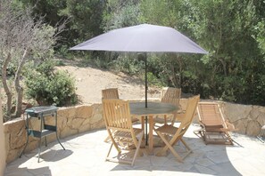 Eine Terrasse im Freien mit einem runden Tisch, vier Holzstühlen, einem großen Sonnenschirm und einem Grill.