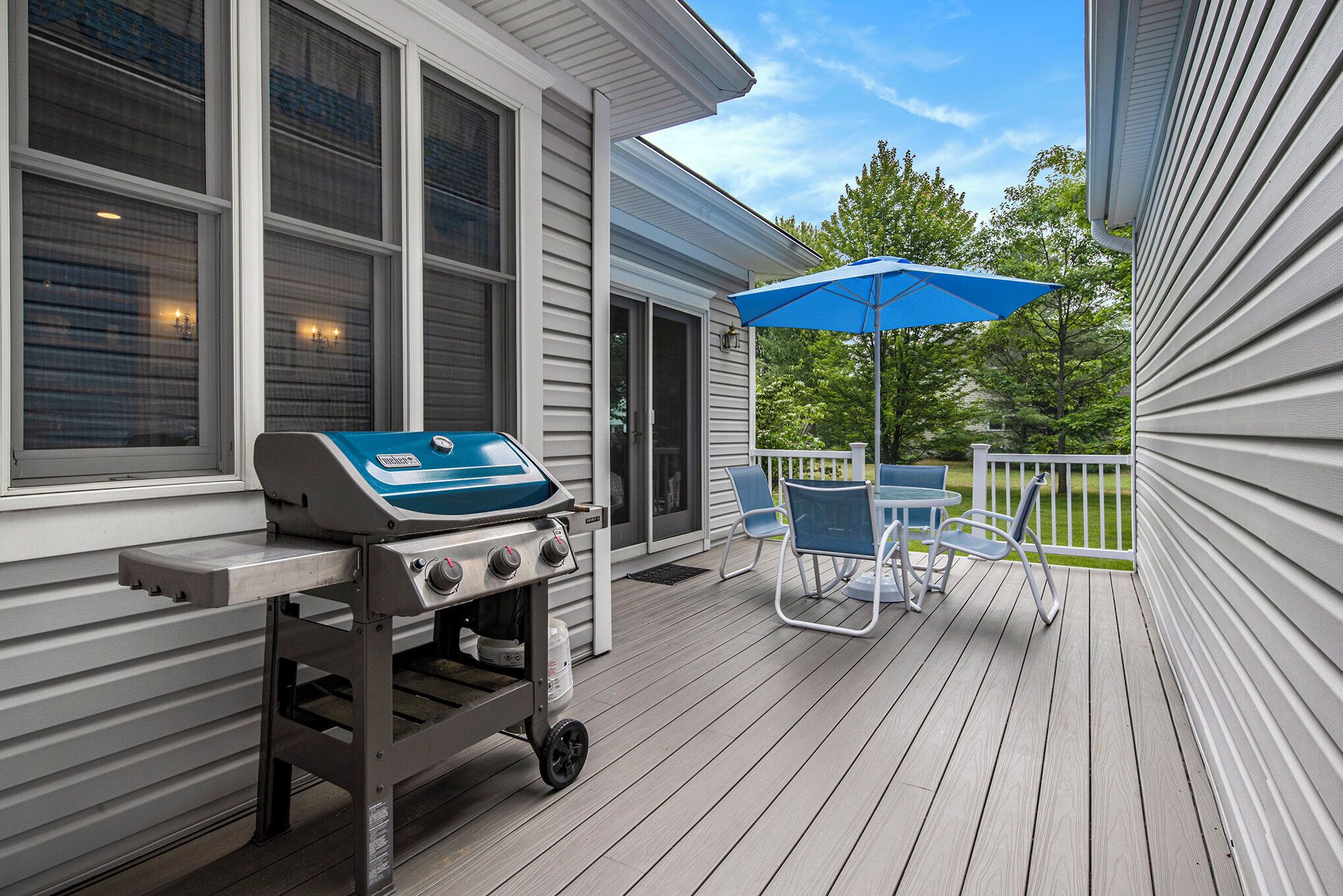 A covered outdoor area with a grill, chairs, and a blue umbrella.