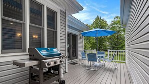 Ein überdachter Außenbereich mit Grill, Stühlen und einem blauen Sonnenschirm.