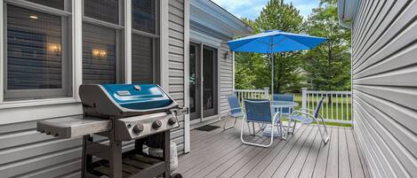 A covered outdoor area with a grill, chairs, and a blue umbrella.