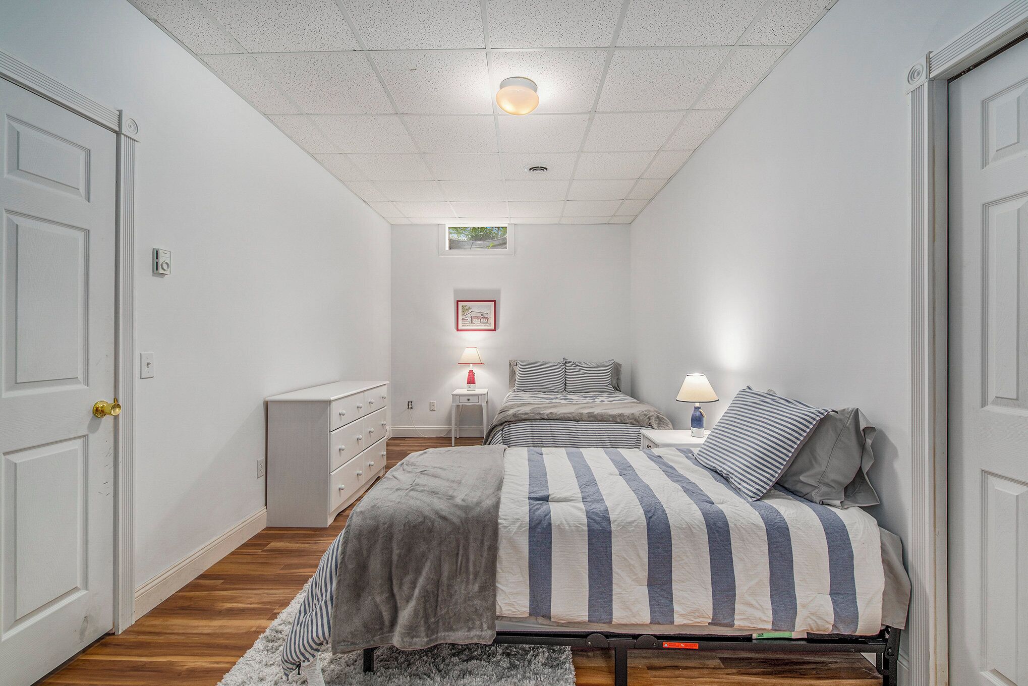 A bedroom with two beds, a nightstand, a dresser, and a small window.