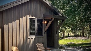 En stuga av trä med två Adirondack-stolar och en eldstad utomhus.