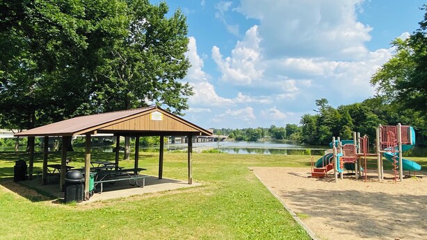 A park with a pavilion, picnic tables, a playground, and a lake in the background. - Blissful Retreat w A trail behind & AC (Wisconsin Rapids)