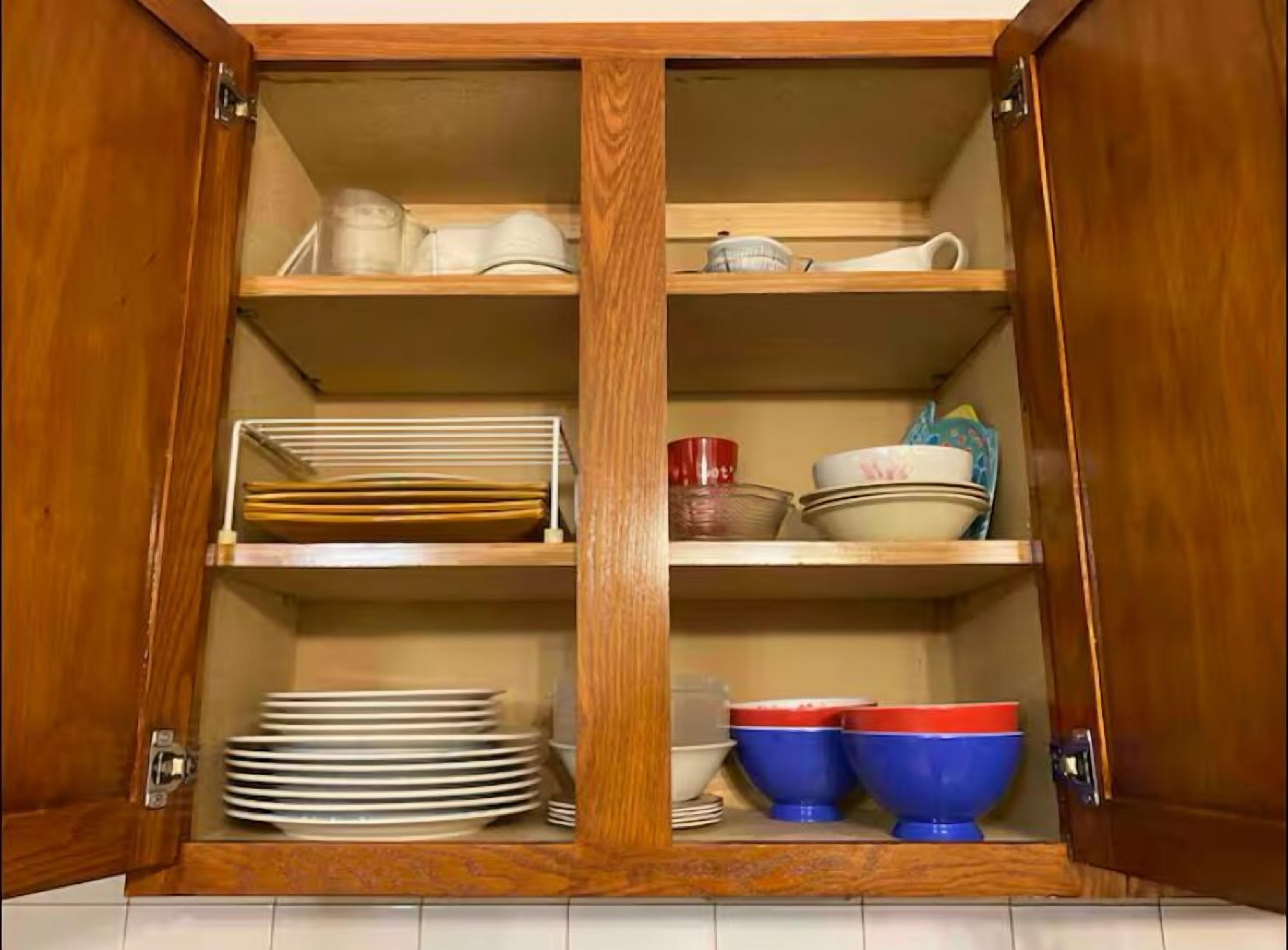 Un armario de madera con tres estantes, cada uno con distintos utensilios de cocina.