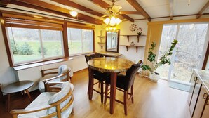 A dining area with a round table, wooden chairs, a ceiling fan, and large windows offering a view of the outdoors. - Blissful Retreat w A trail behind & AC (Wisconsin Rapids)