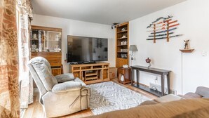 A living room with a TV, a sofa, a wooden entertainment unit, and a decorative wall piece. - Blissful Retreat w A trail behind & AC (Wisconsin Rapids)