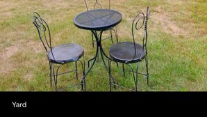 A yard with a small round table and two chairs, surrounded by lush greenery and a large bush with white flowers. - Blissful Retreat w A trail behind & AC (Wisconsin Rapids)