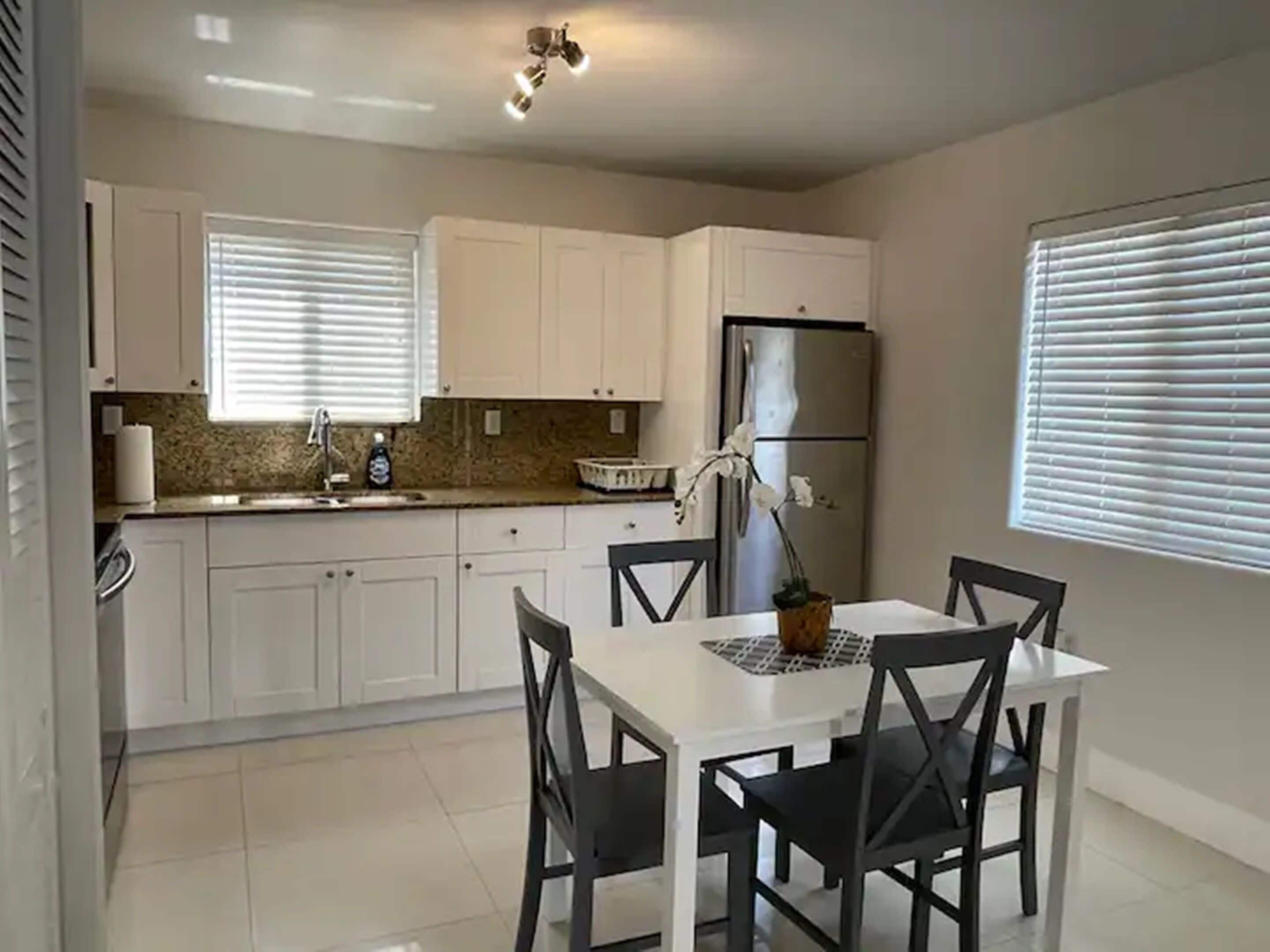 Una cocina moderna con armarios blancos, un refrigerador de acero inoxidable y una mesa de comedor con sillas negras.