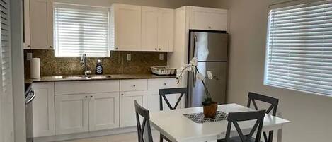 Una cocina moderna con armarios blancos, un refrigerador de acero inoxidable y una mesa de comedor con sillas negras.