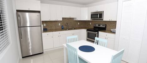 Una cocina moderna con armarios blancos, electrodomésticos de acero inoxidable y una mesa de comedor blanca con sillas azules.