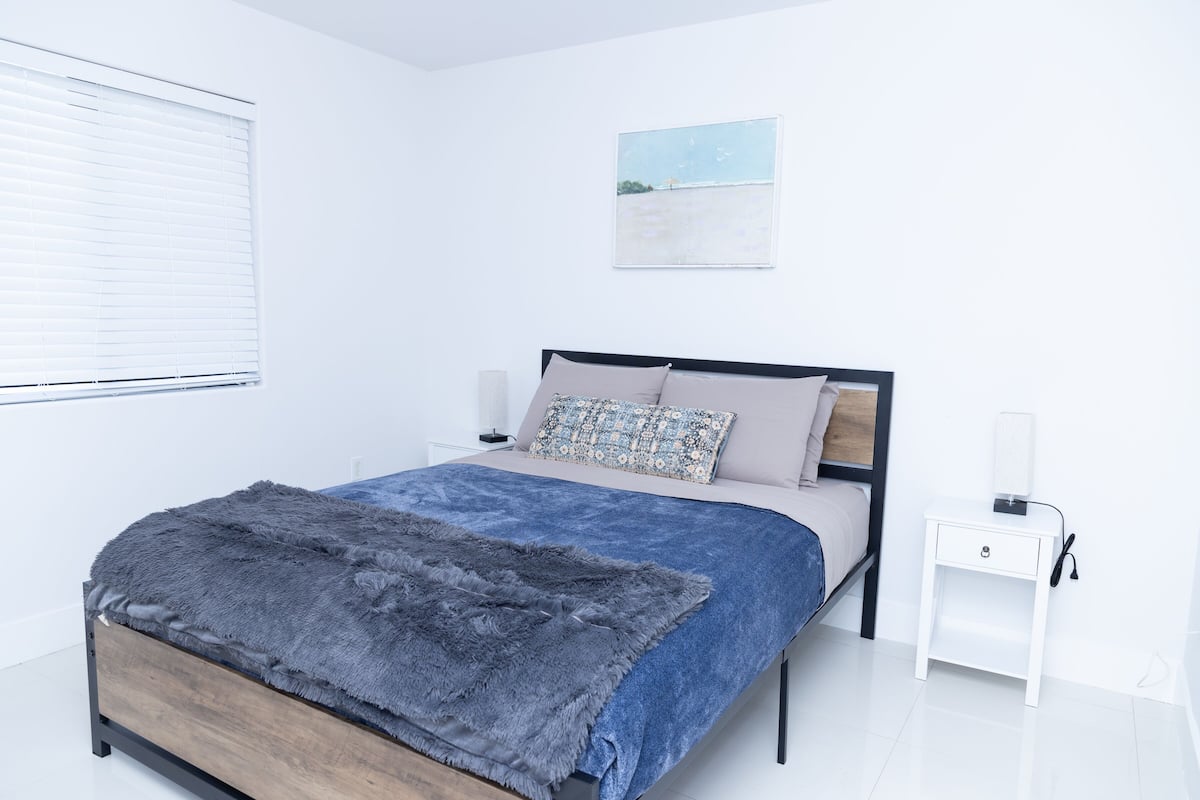 A modern bedroom with a bed, a nightstand, a lamp, and a painting on the wall.