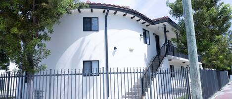 A two-story house with a white exterior, a red-tiled roof, and a black metal fence.