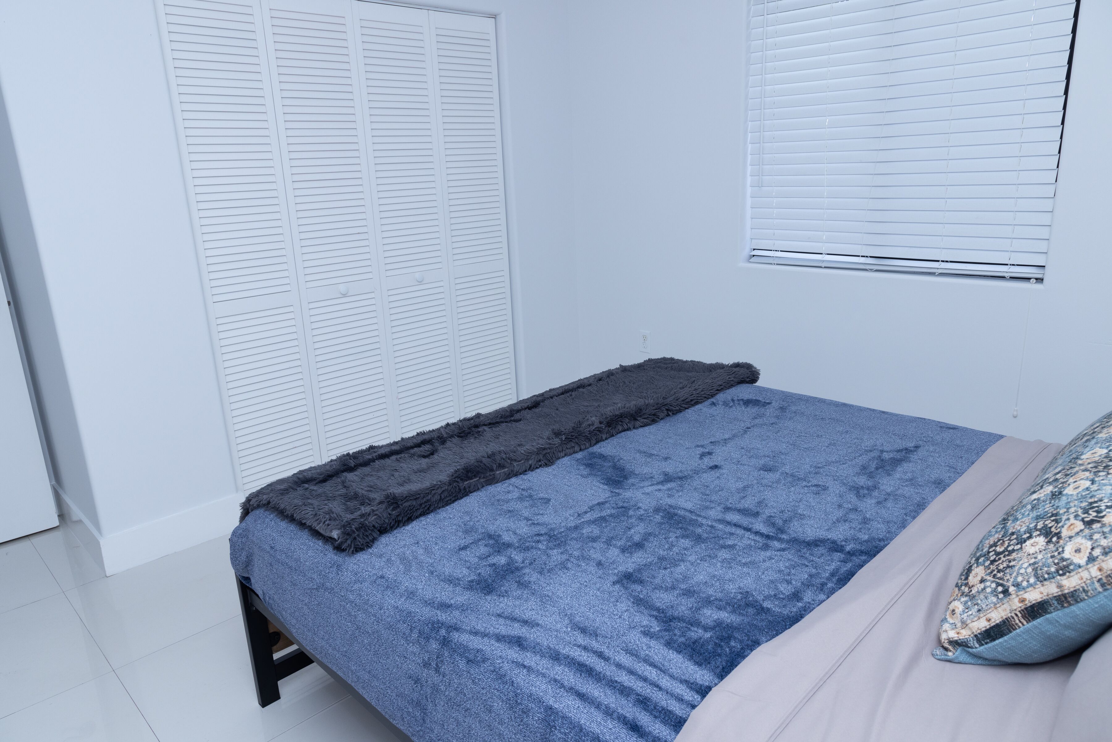 A bedroom with a bed, a wardrobe, and a window with blinds.