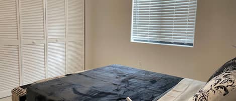 Quarto com cama, janela com persianas e guarda-roupa com portas venezianas.