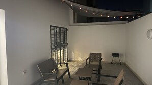 Uma área de pátio com mesa e cadeiras, uma janela com grade de metal e luzes de fada.