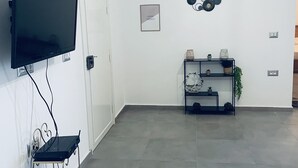 Uma sala de estar moderna com televisão de tela plana na parede, um rack preto com objetos decorativos e piso em azulejos.