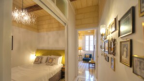 A hotel room with a bed, a chandelier, and a hallway with framed pictures. - Traditional & chic 2 bedrooms in Valletta IMCD1-1 (Valletta)