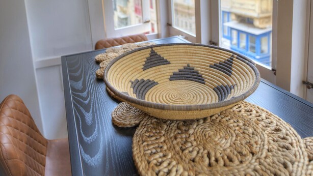 A room with a view of buildings through large windows, a table with woven placemats, and a leather chair. - Traditional & chic 2 bedrooms in Valletta IMCD1-1 (Valletta)