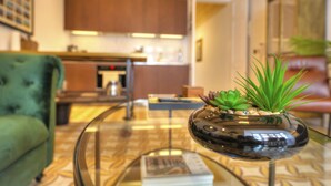 A modern living room with a glass coffee table, a green armchair, and a kitchen in the background. - Traditional & chic 2 bedrooms in Valletta IMCD1-1 (Valletta)