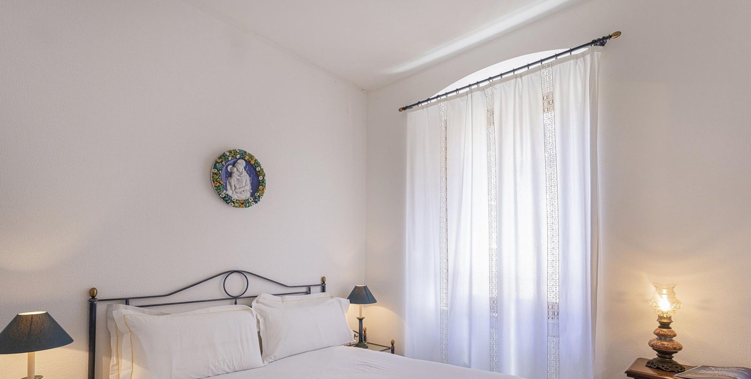 Een slaapkamer met een bed, twee bedlampjes, een decoratief bord aan de muur en een gordijn.