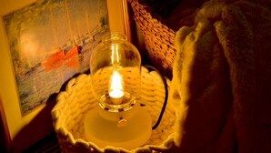 Een knus ingerichte kamer met een lijstwerkschilderij, een brandende kaars in een gevlochten mand en een zachte, pluizige deken.