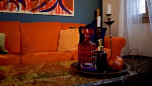 Een kamer met een oranje bank, een tafel met een fles en een appel, en een schilderij aan de muur.