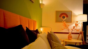 Een hotelkamer met een bed, kussens, een nachtkastje met een lamp, een vaas met bloemen en een wanddecoratie.
