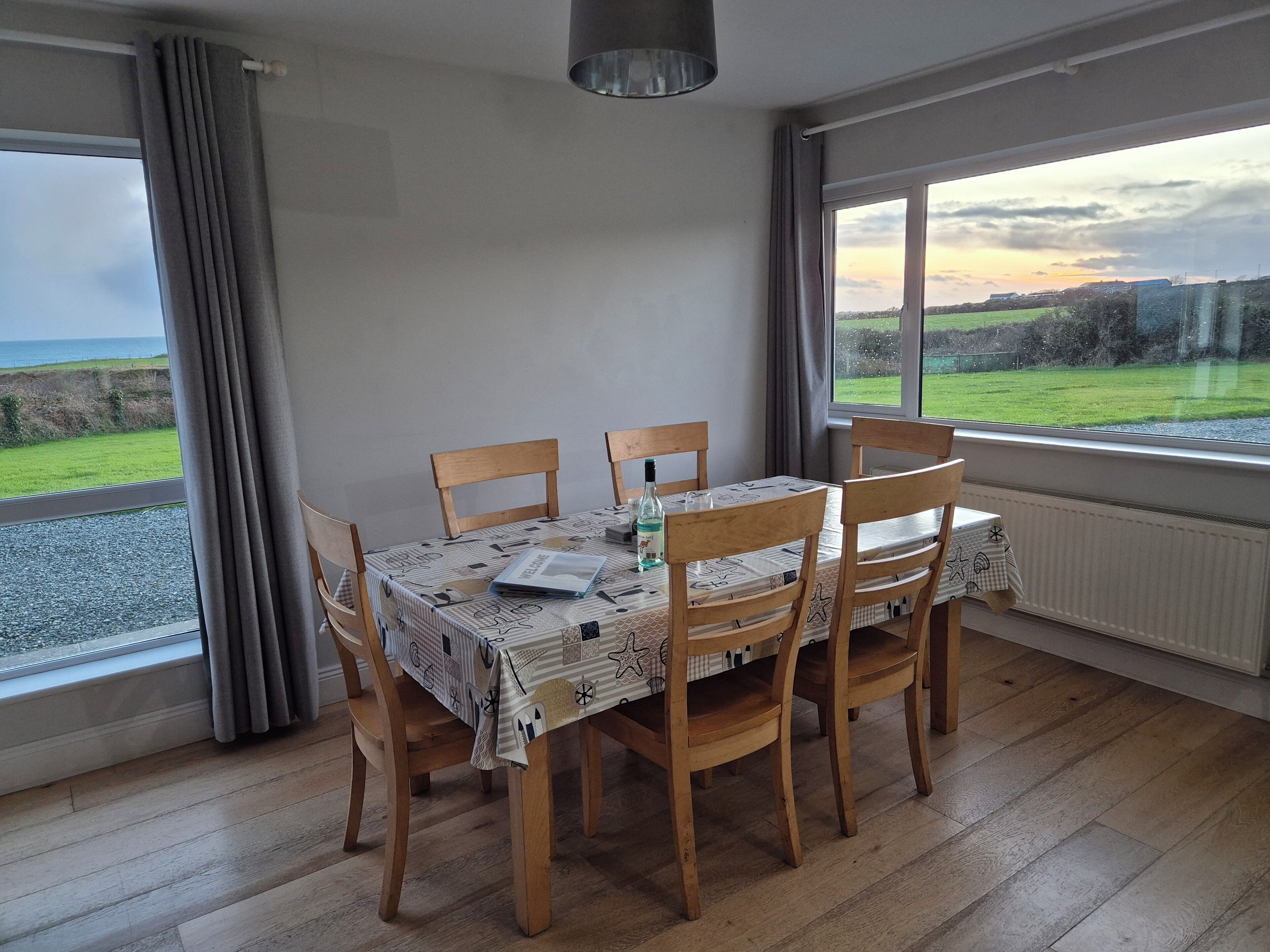 A dining area with a table set for four, wooden chairs, and a view of the sea through large windows.