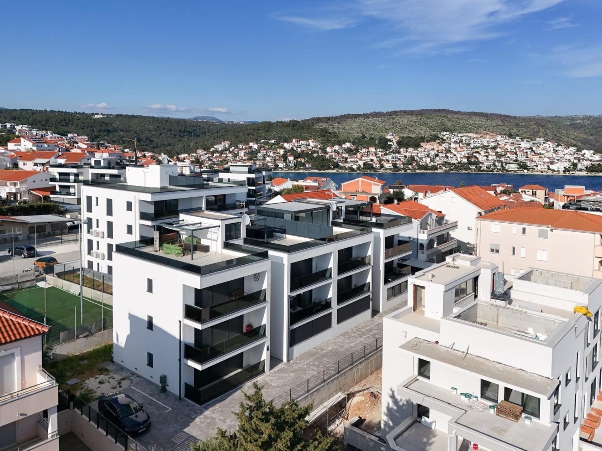 Una zona residencial moderna con edificios de varios pisos, vista despejada al mar y un paisaje montañoso al fondo.