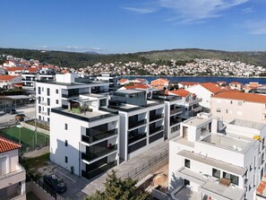 A modern residential area with multi-story buildings, a clear view of the sea, and a hilly landscape in the background. - Apartment Summer Breeze Okrug Gornji (Okrug)