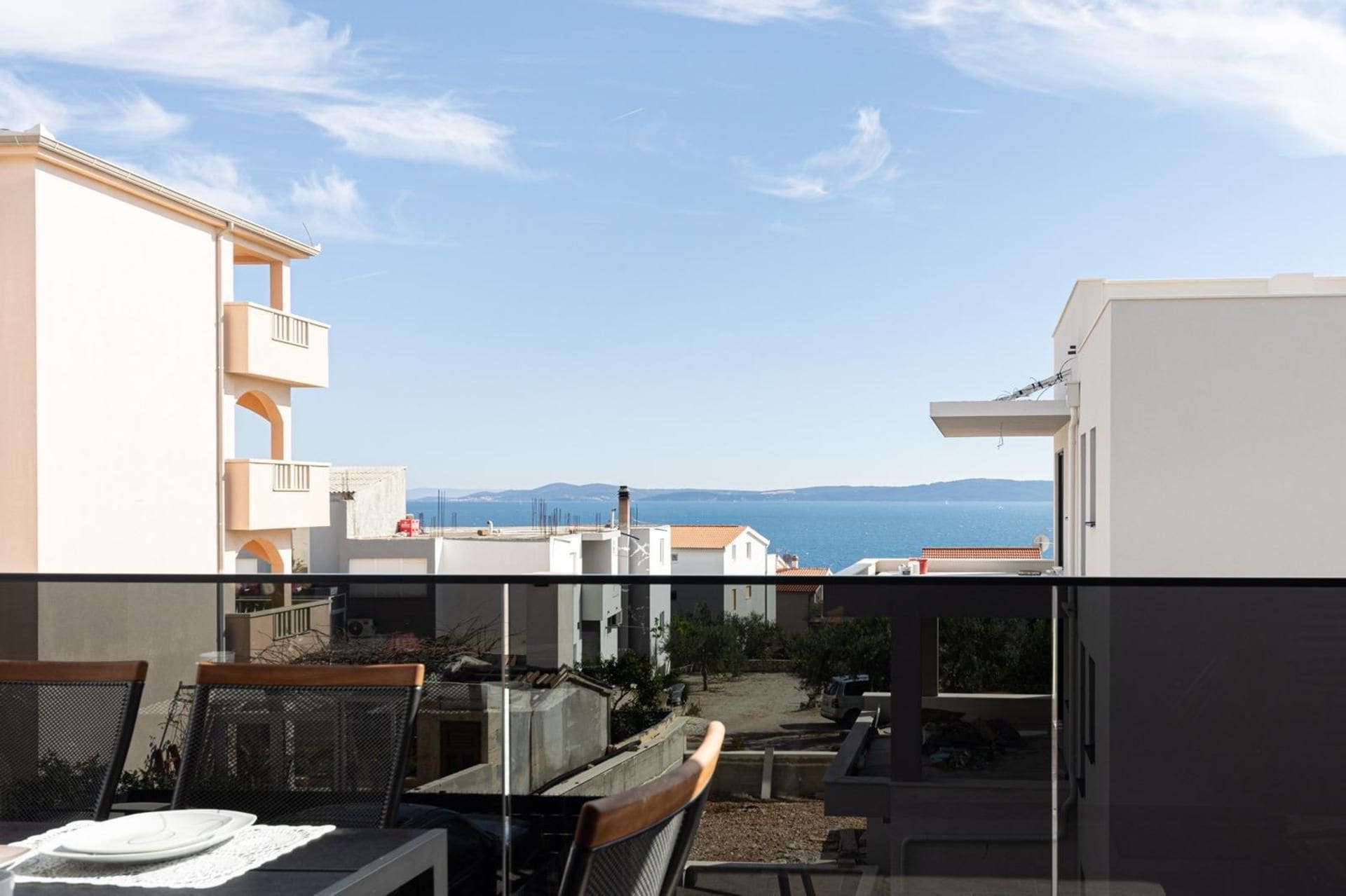 A balcony with a view of a coastal town, a dining table with chairs, and a clear sky.