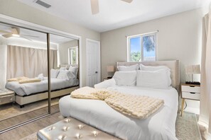 Un dormitorio moderno con una cama grande, un espejo, una ventana y un ventilador de techo.