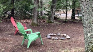 A forested area with two chairs, one red and one green, and a circle of rocks on the ground. - This is what “Up North” feels like! (Lewiston)