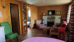 A cozy living room with wooden walls, a fireplace, a green chair, a leather armchair, and a red table. - This is what “Up North” feels like! (Lewiston)