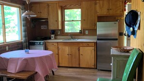 A kitchen with wooden cabinets, a stainless steel refrigerator, a stove, and a dining table with a checkered tablecloth. - This is what “Up North” feels like! (Lewiston)