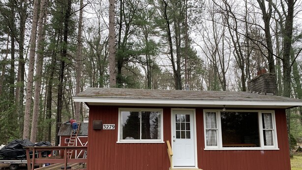 A small, single-story cabin with a red exterior and white trim, numbered 3279, surrounded by a forest. - This is what “Up North” feels like! (Lewiston)