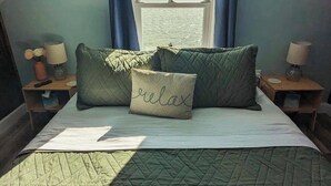 Un dormitorio con cama, dos mesitas de noche, una ventana con cortinas y vistas al mar.