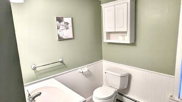 A bathroom with a white sink, toilet, and cabinet, a framed picture on the wall, and a light fixture.
