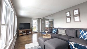 Una sala de estar con un sofá grande de color gris, un mueble de entretenimiento de madera y un televisor.