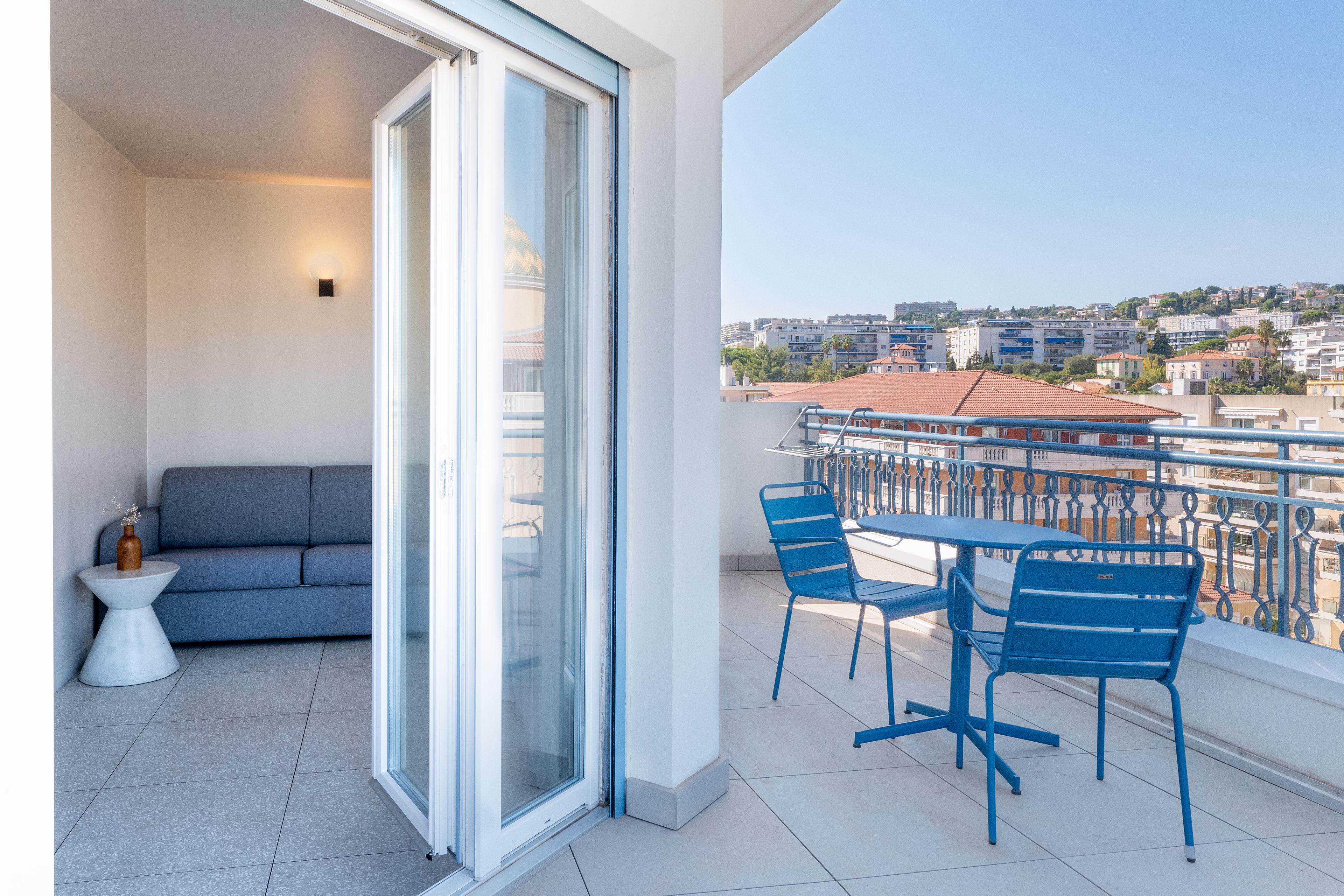 A balcony with a sofa, a table, and chairs, overlooking a cityscape.