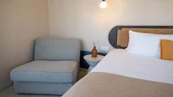 A hotel room with a bed, a grey armchair, a bedside table with a vase, and a hanging light fixture.