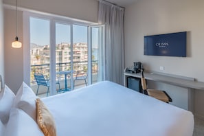 Une chambre d’hôtel comprenant un lit, une télévision, un bureau avec une chaise et un balcon avec des chaises.
