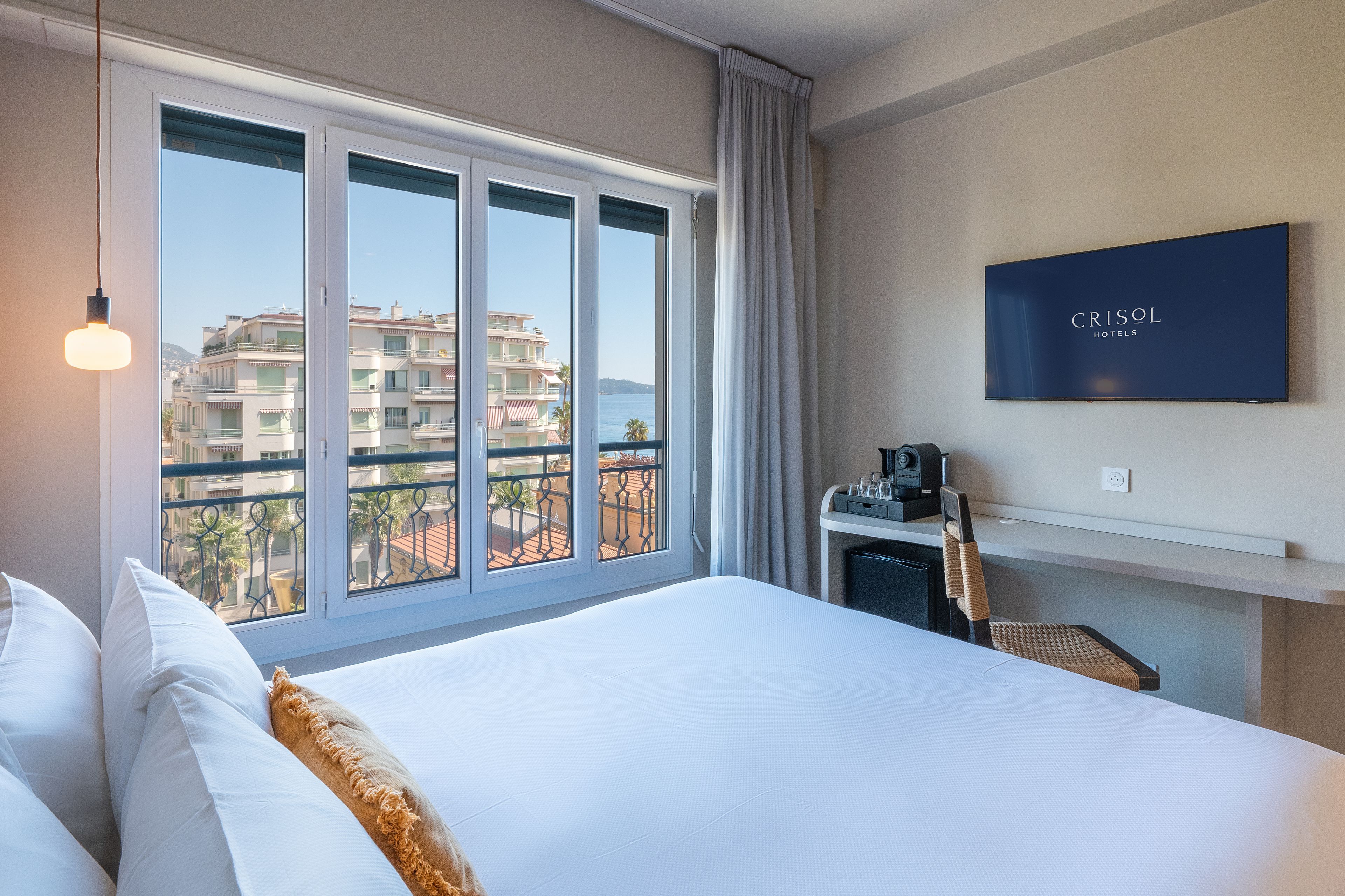 A hotel room with a large bed, a desk with a coffee machine, and a TV displaying 'CRISOL HOTELS'.