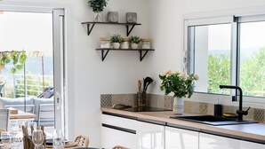 A modern kitchen with a wooden dining table set for six, a black countertop, and a window with a view of greenery. - Splendid villa with swimming pool & sea view (Roquebrune-sur-Argens)