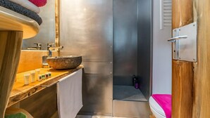 A modern bathroom with a wooden vanity, a large mirror, a stone basin, and a shower area.