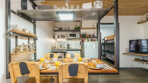 A compact kitchen with a dining area, featuring a wooden table, chairs, and a TV on a shelf.